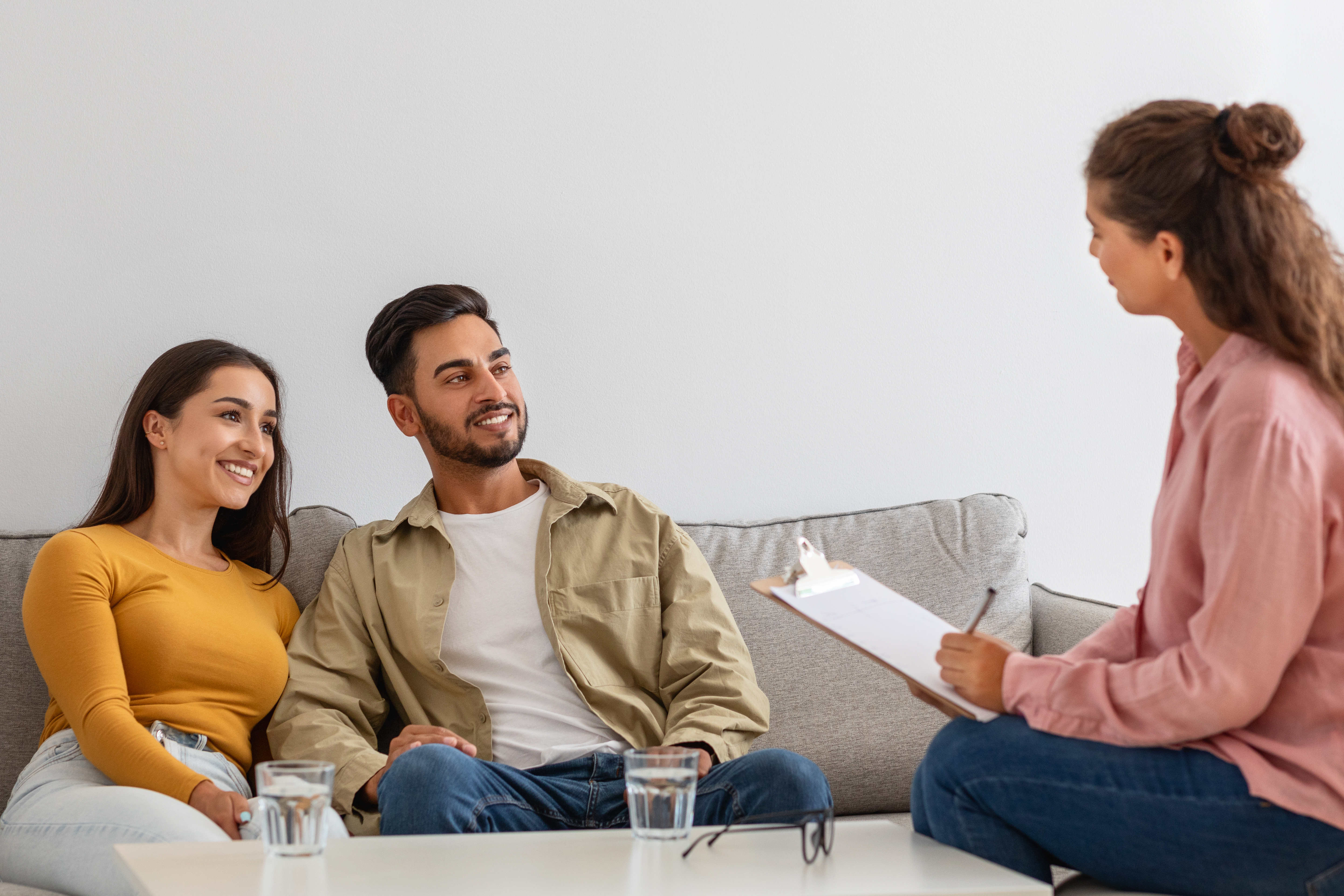 A smiling couple seated on a couch while listening to their couples therapist.