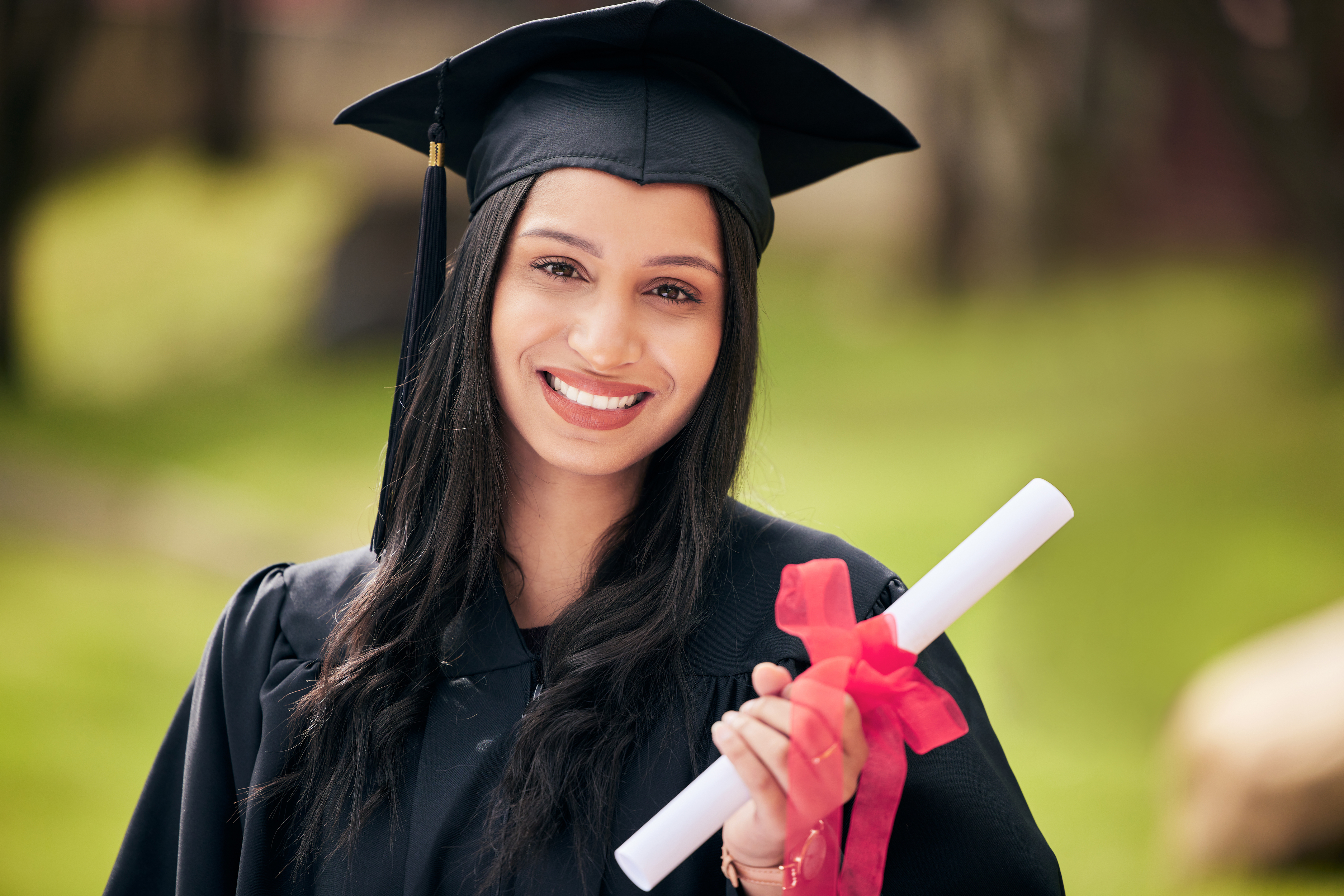A master’s graduate wearing a cap and gown smiles.