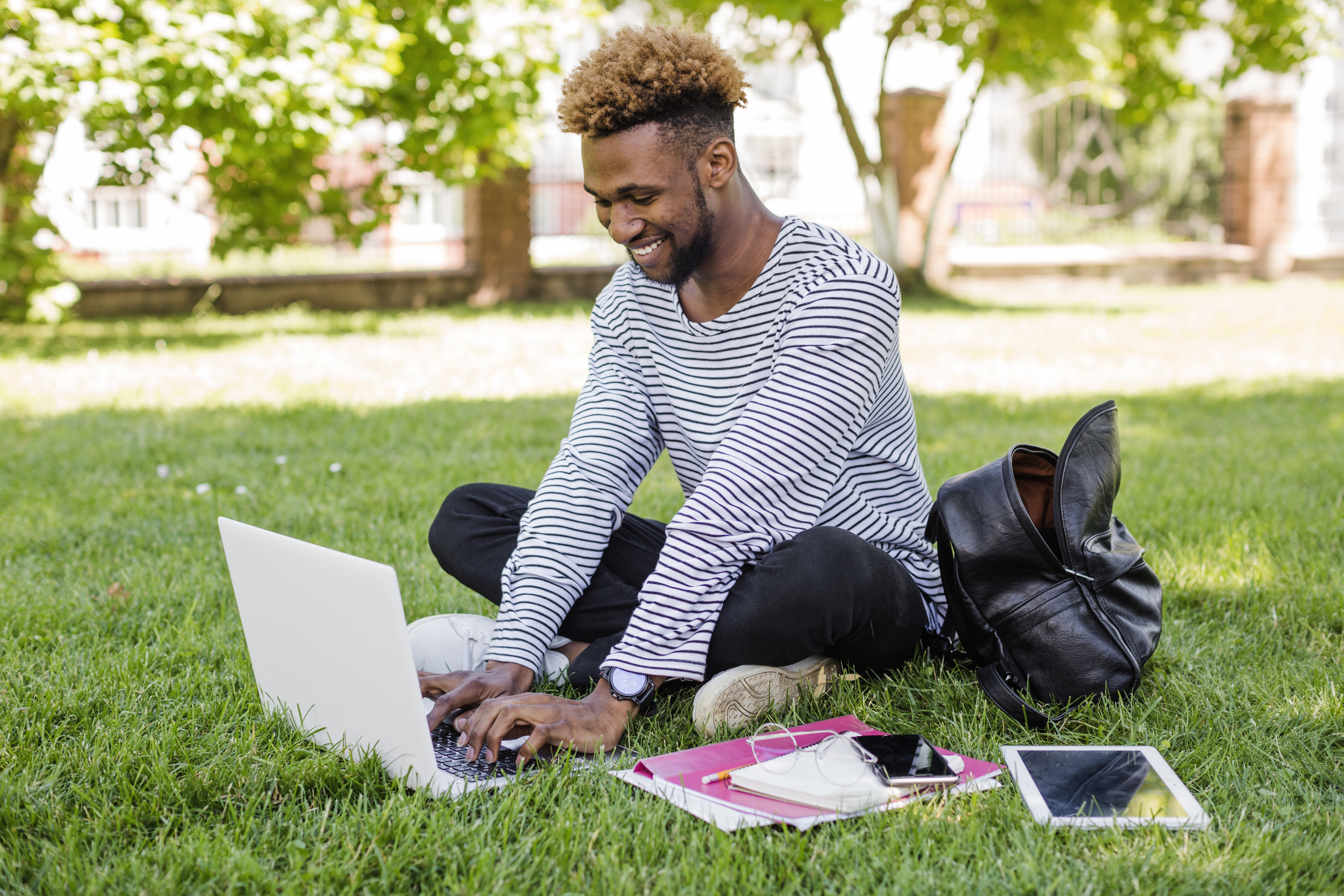 Online student working on a laptop in a park.