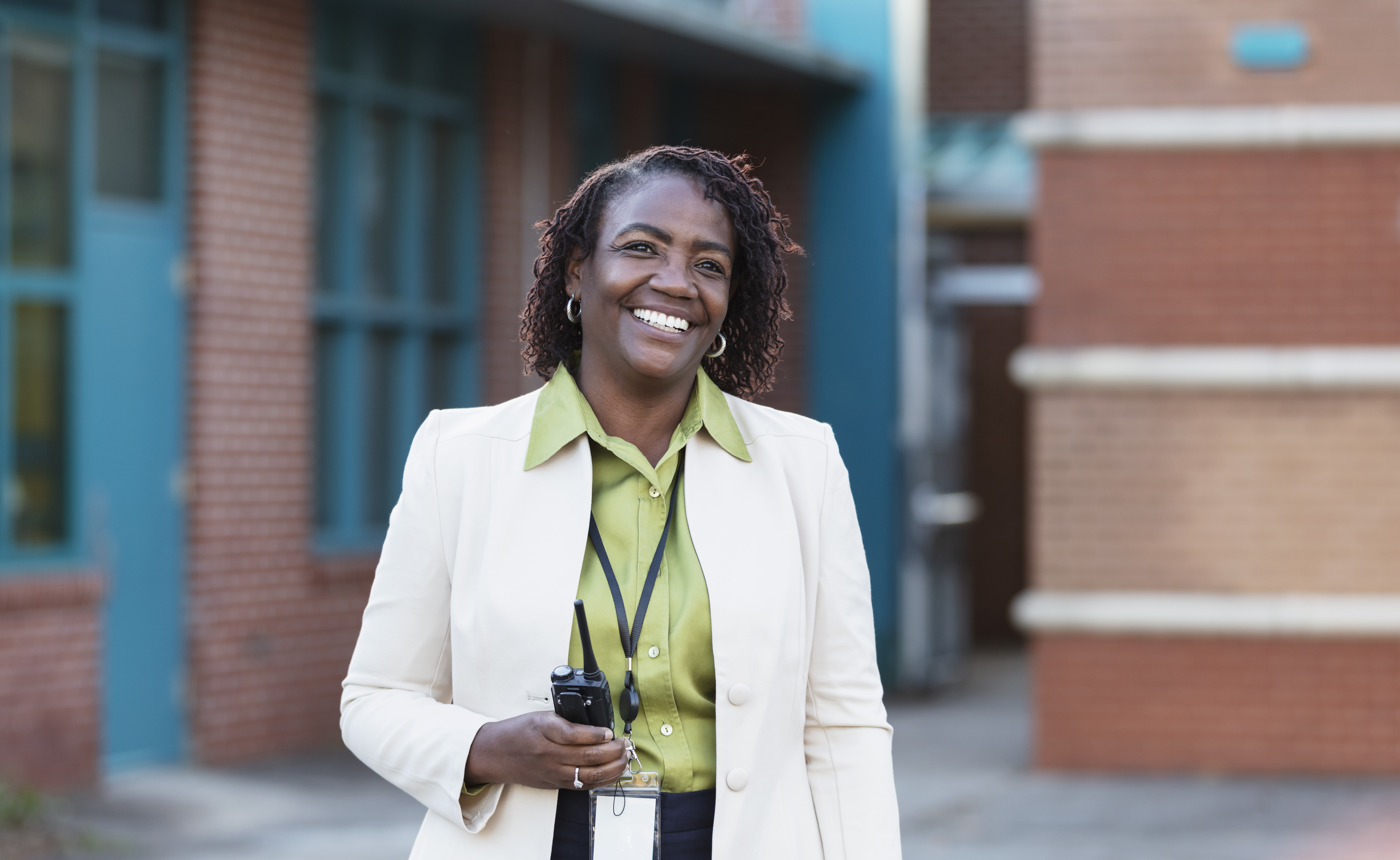 A mature African-American school principal standing outside a school building and smiling.