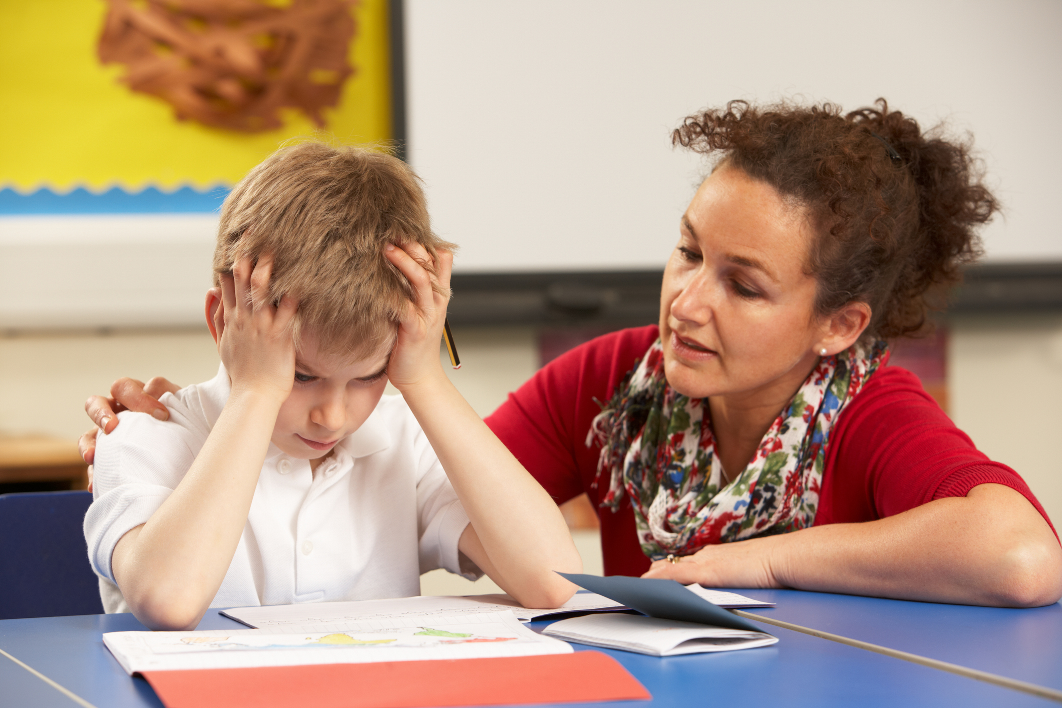 Frustrated school boy working with teacher in the classroom