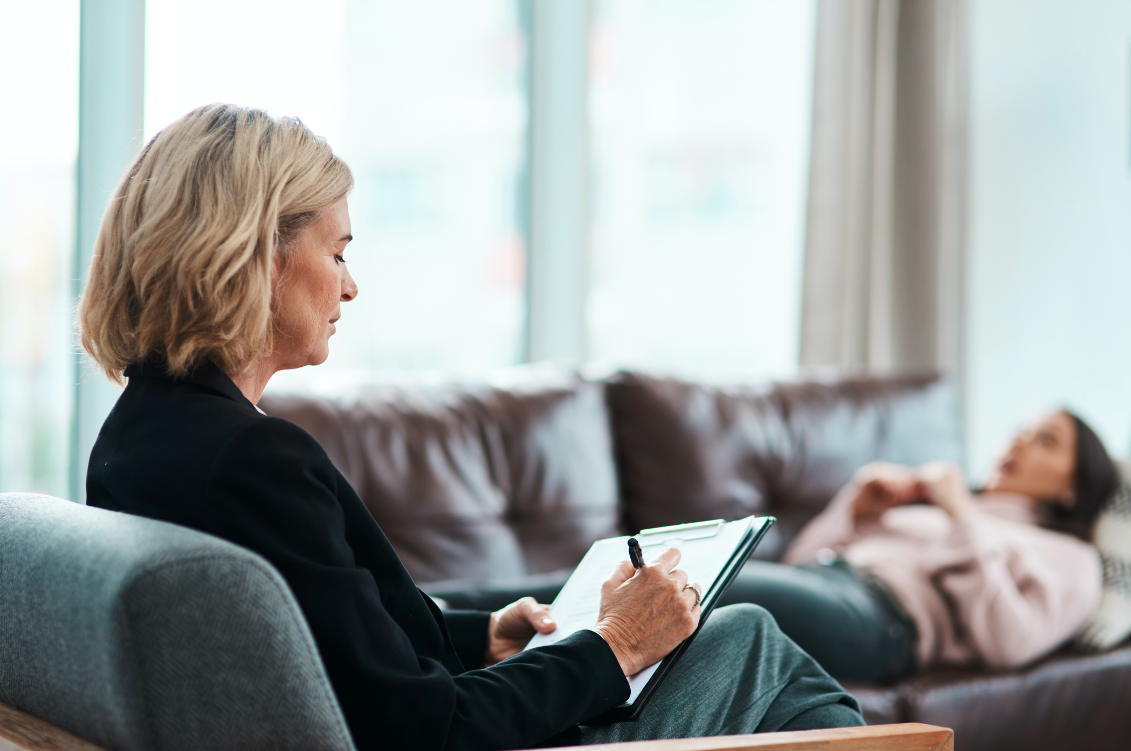 A mature psychologist writing notes during a therapeutic session with her patient