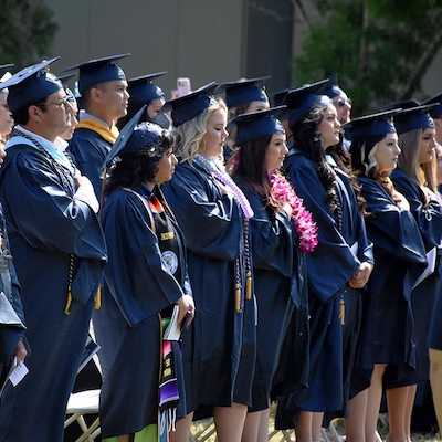 A group of graduates standing in dark blue graduation regalia.