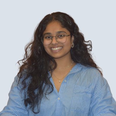 A student smiling in front of a light blue wall.