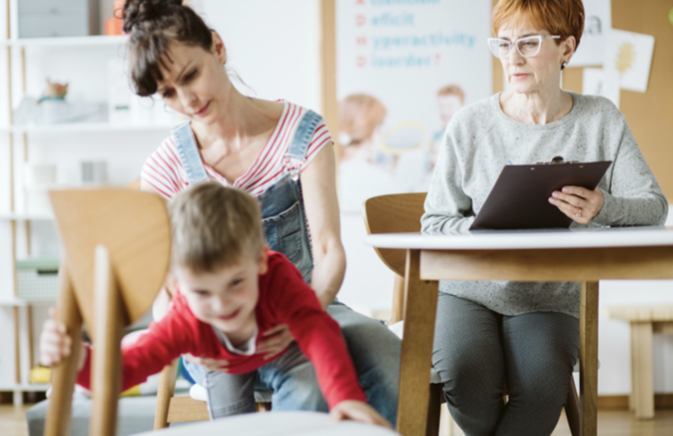Educational therapist watching a parent hold a child reaching for another chair. 
