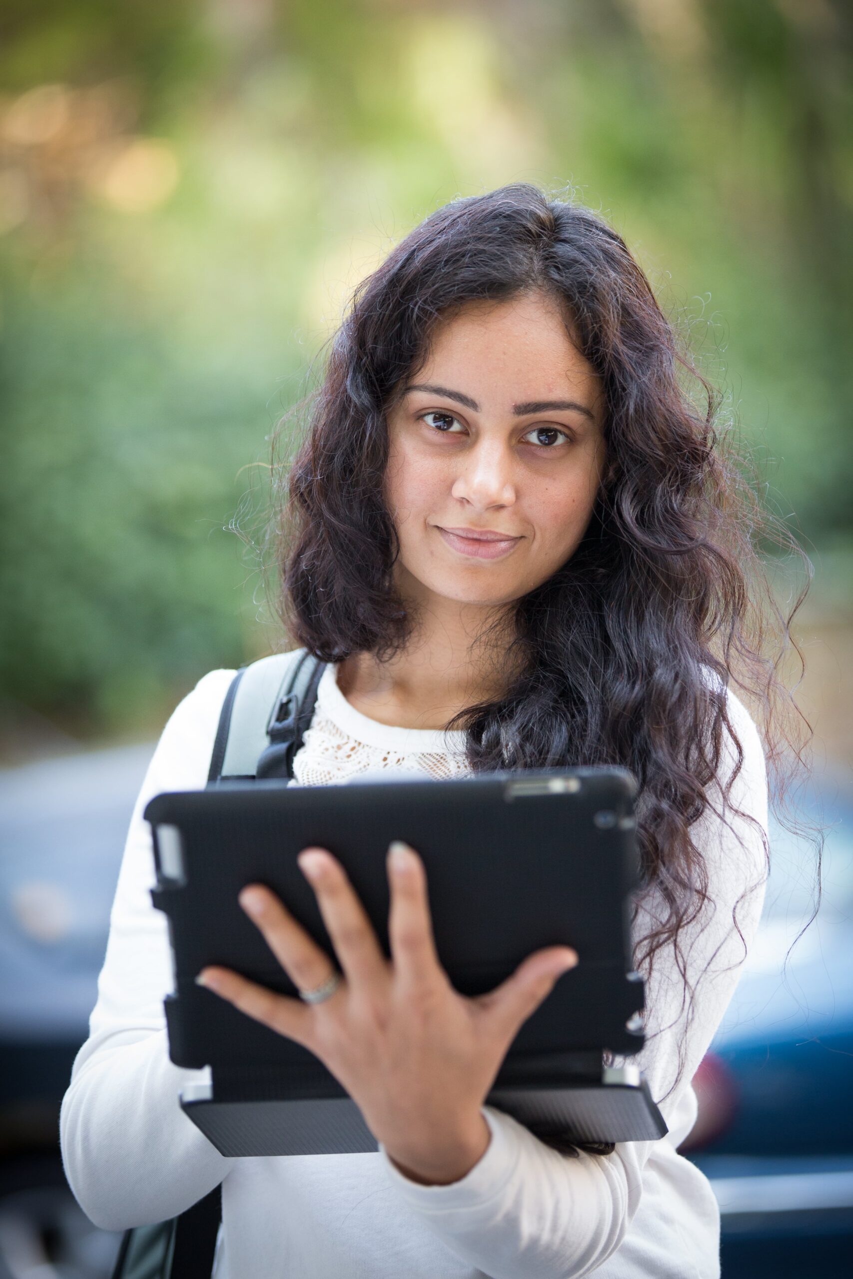 A bachelor’s degree student wearing a backpack holds a tablet.